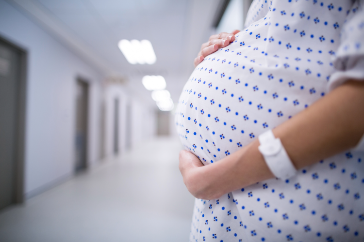pregnant woman holds bump in a hospital ward gown